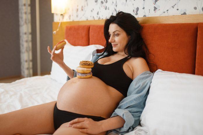 Pregnant woman with belly eats cakes in bed