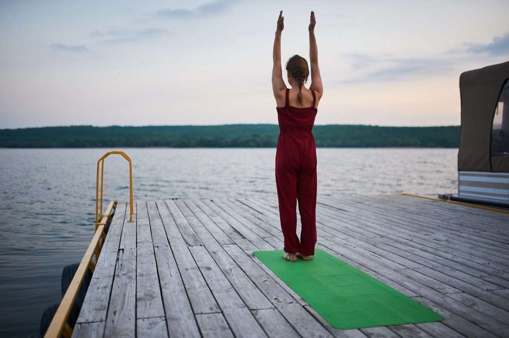 Beautiful young woman practices yoga asana Tadasana - Mountain pose on the wooden deck near the lake