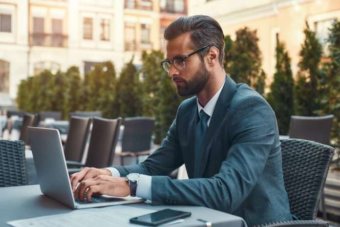 Modern businessman. Portrait of handsome bearded businessman in eyeglasses working with laptop while