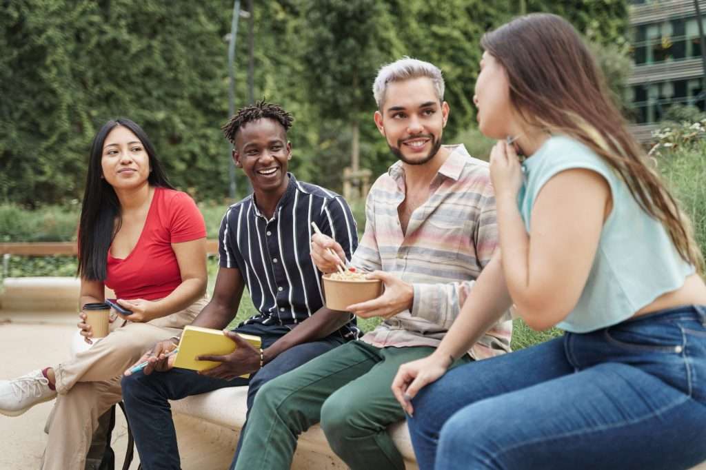 young cosmopolitan friends or colleagues enjoying conversation while eating take away street food