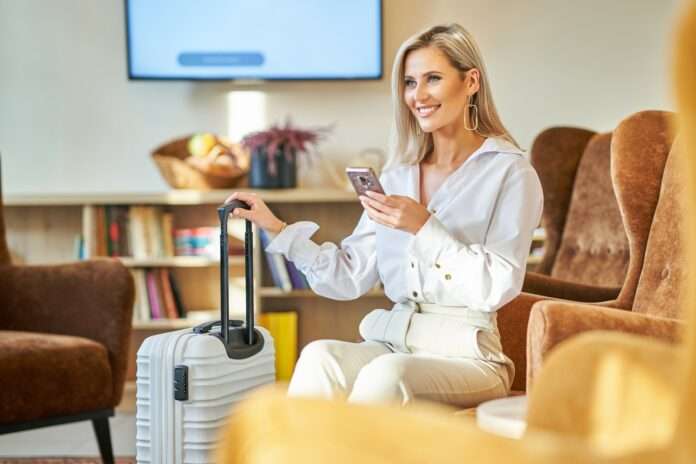 Businesswoman with luggage in modern hotel lobby using smartphone