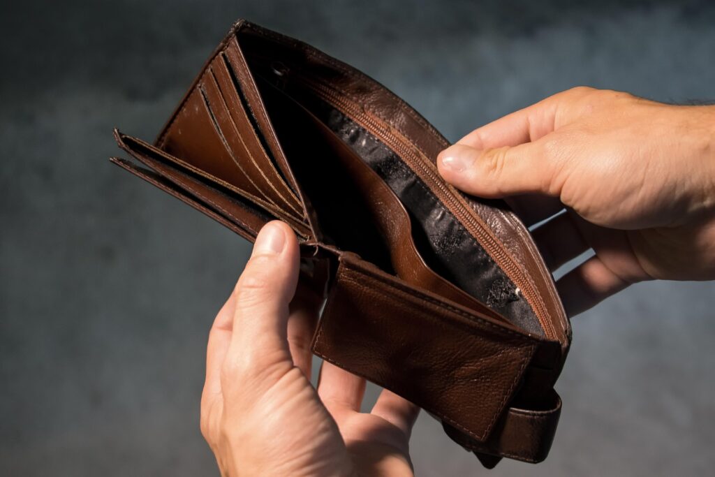 Close-up of hands holding an empty brown wallet, highlighting the impact of daily spending and lack of savings.