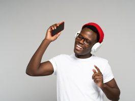 African American man with headphones enjoying listening to music, dances, holding mobile phone