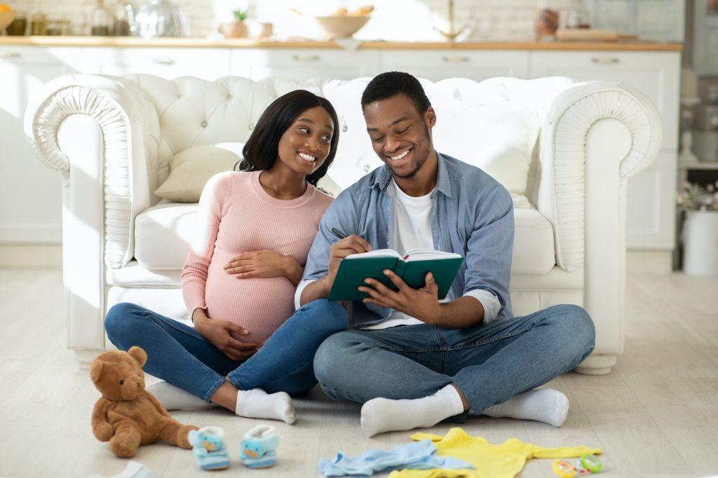 Happy black couple making checklist of baby things for maternity hospital at home