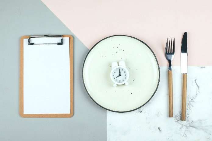 Intermittent fasting, ketogenic, diet concept. Plate with white alarm clock and white notepad