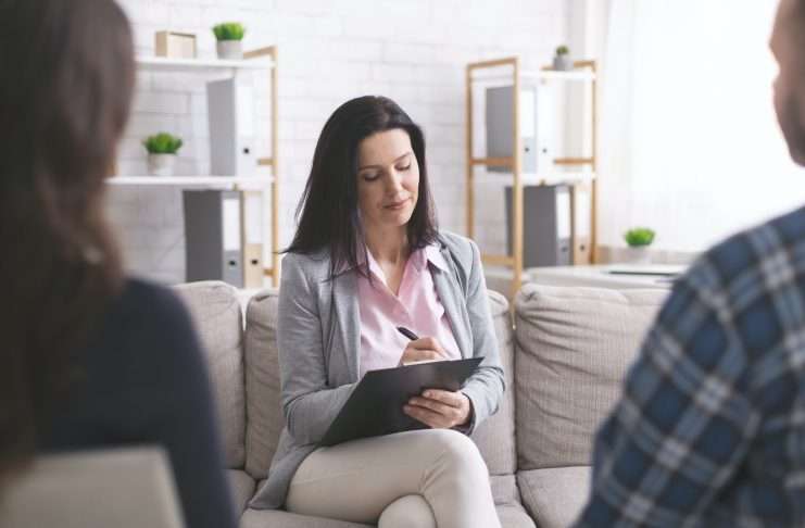 Professional psychologist taking notes at couple meeting with patients