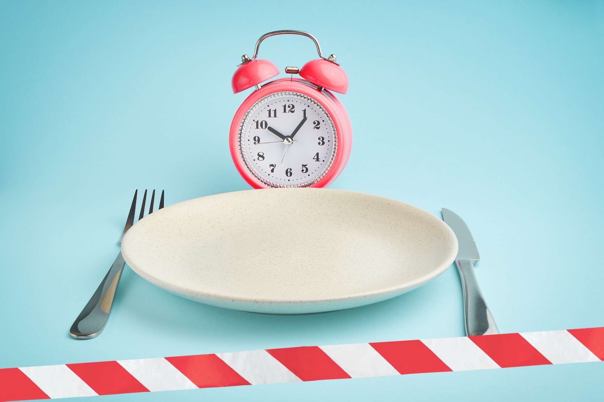 Alarm clock, plate and barrier tape. intermittent fasting, lunchtime, diet and weight loss