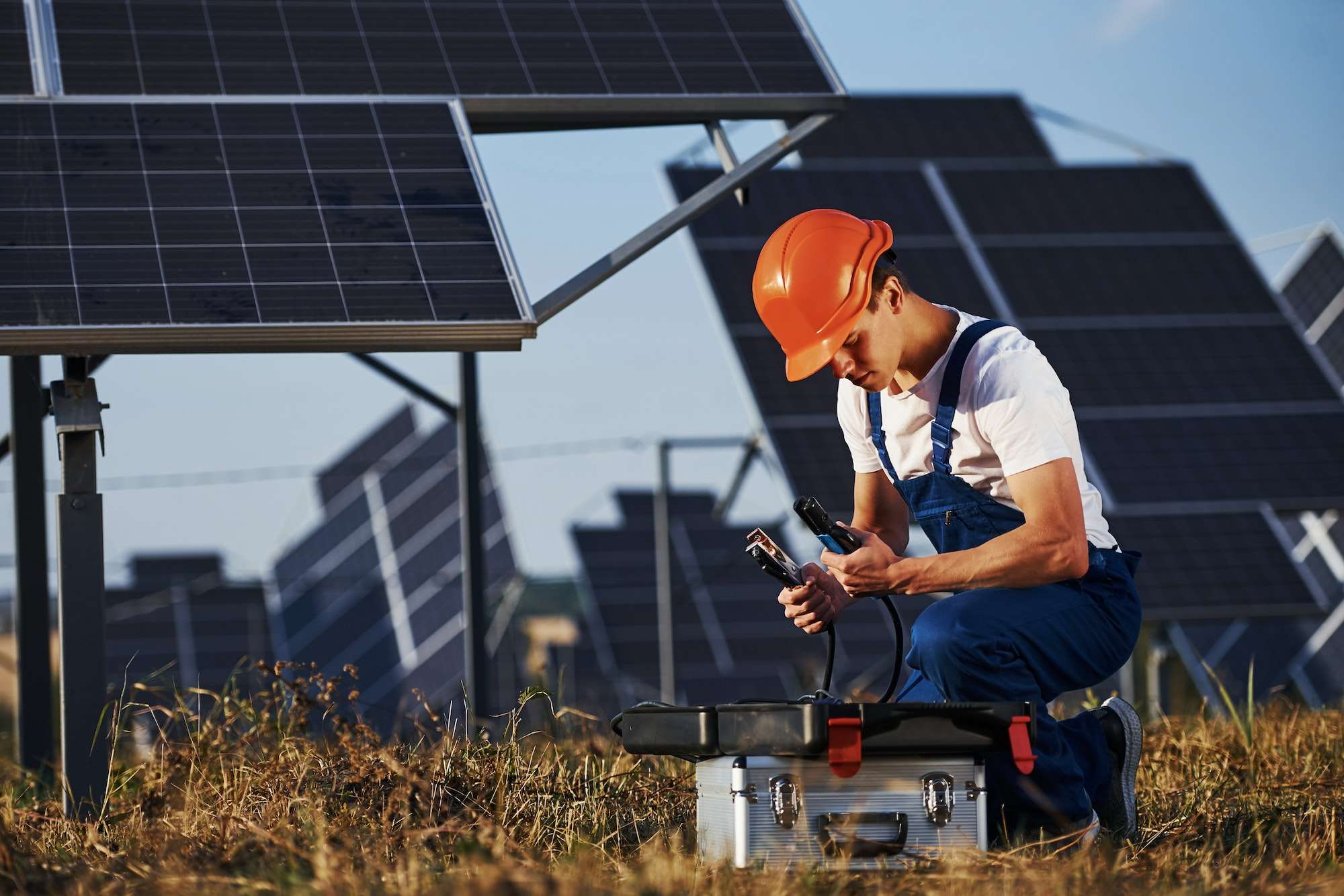 Male worker in blue uniform outdoors with solar batteries at sunny day