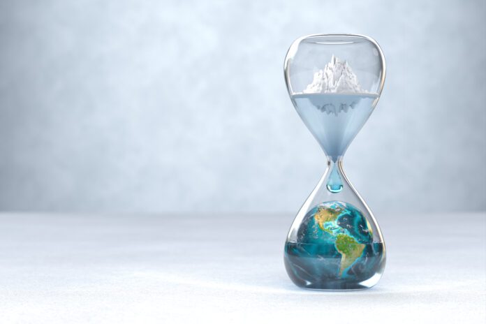 A conceptual image of an hourglass where the top chamber contains a melting iceberg and the bottom chamber holds the Earth partially submerged in water, with a droplet falling between them, symbolizing climate change and rising sea levels over time.